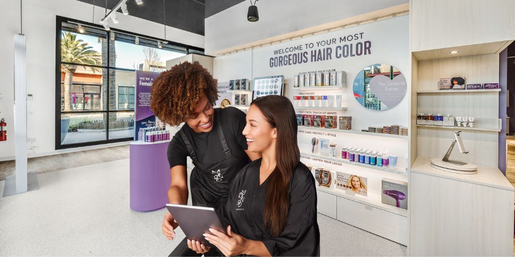 Stylist and client smiling while viewing hair color options on a tablet in a modern salon."