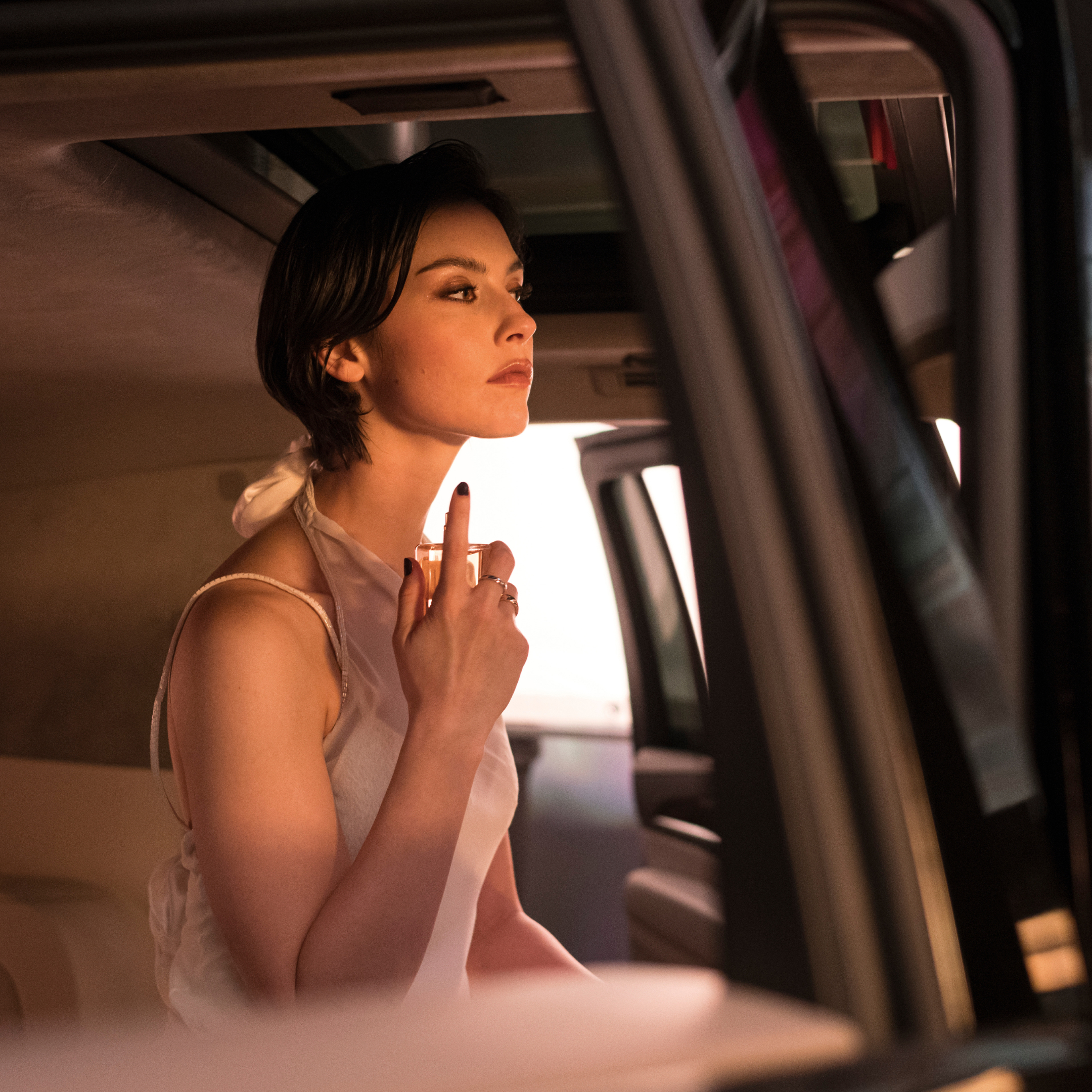 woman spritzing herself with perfume in the back of a car