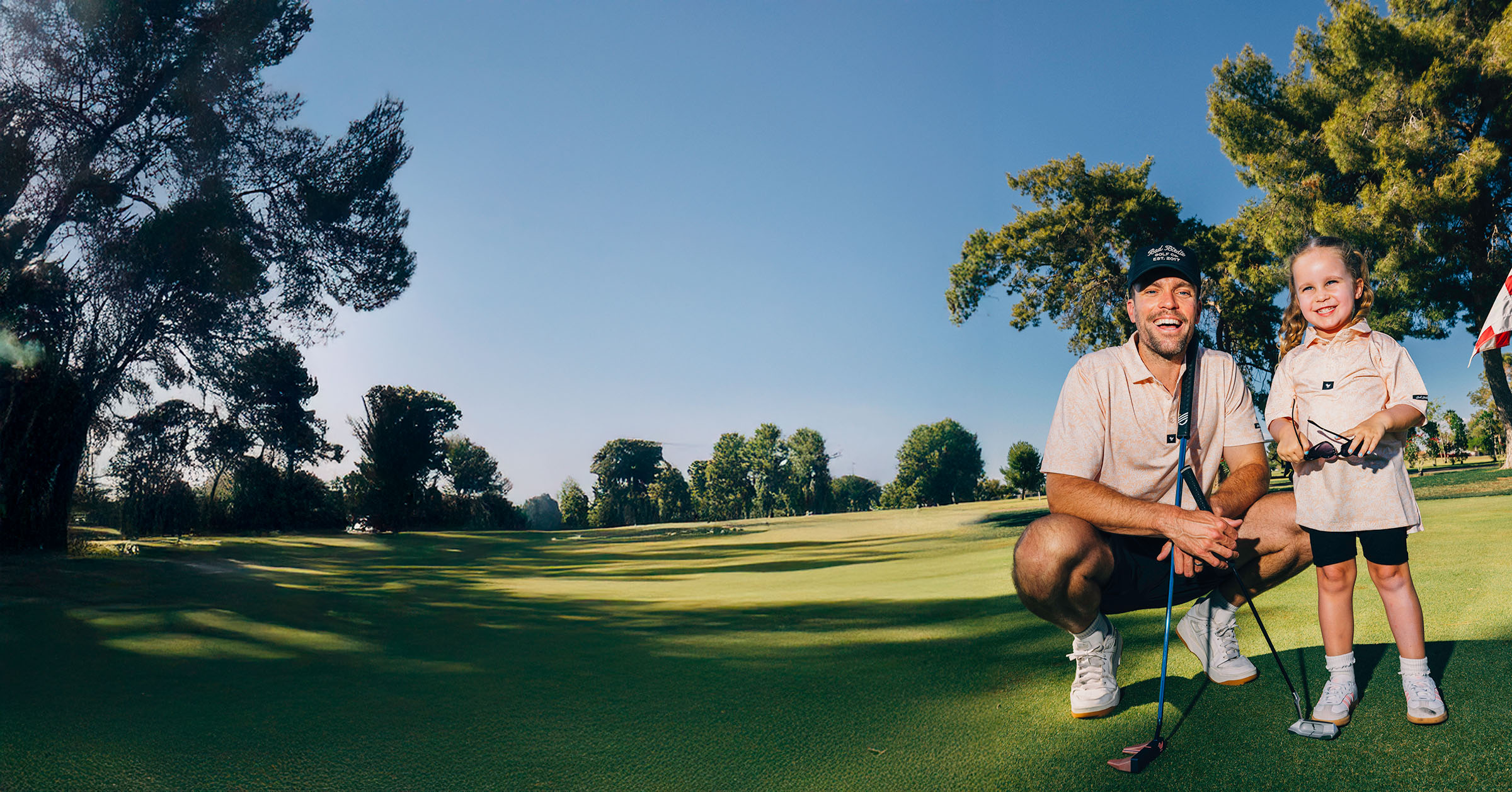 Man and young girl in matching polos smiling on a golf course.