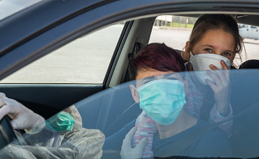 Two people in car with window half-way down wearing masks