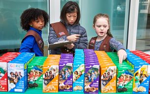 three girls selling girl scout cookies