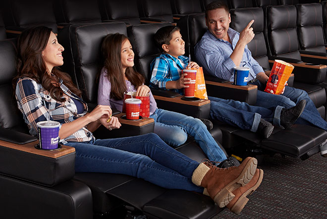 Family of four sitting with their legs extended in the harkins electronic reclining chairs with popcorn and soda.
