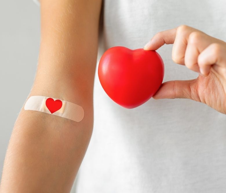 Person's arm with a heart bandaid and holding a heart in their other hand