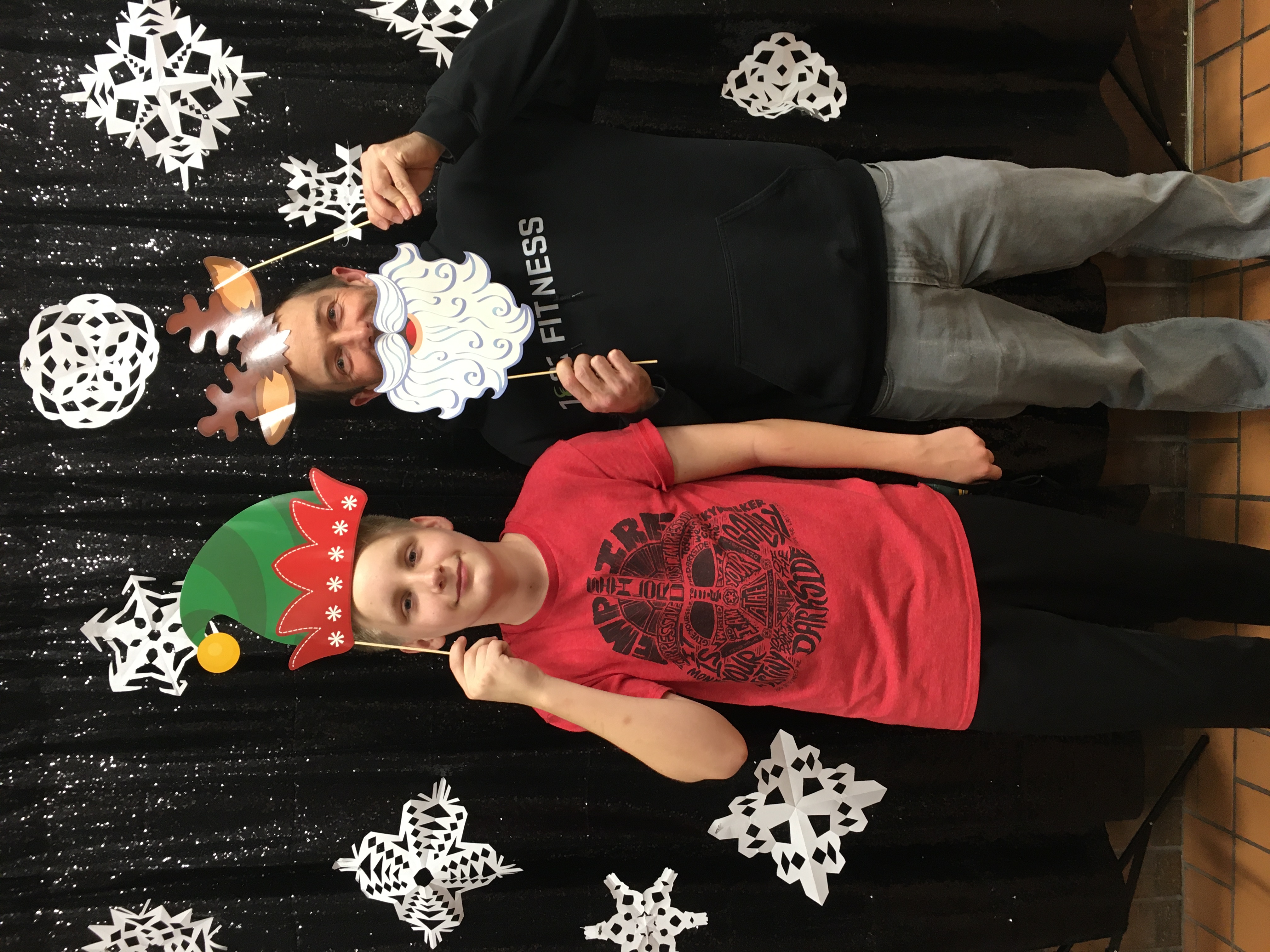 Two males standing in front of snowflakes with an elf hat and reindeer antlers 
