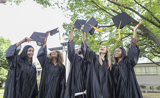 Five students in black cap and gowns, throwing their caps in the air.