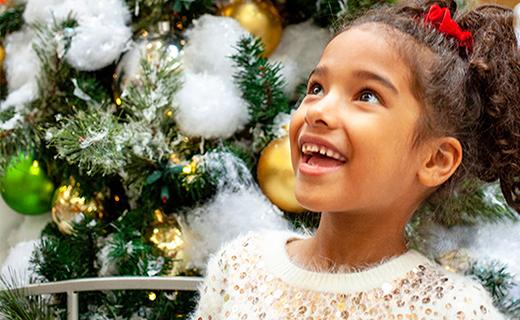 Young girl looking up and smiling with a Christmas tree in background