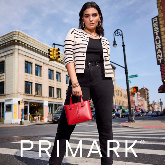 Woman standing in black jeans and tank top, with white and black strip jacket for Primark