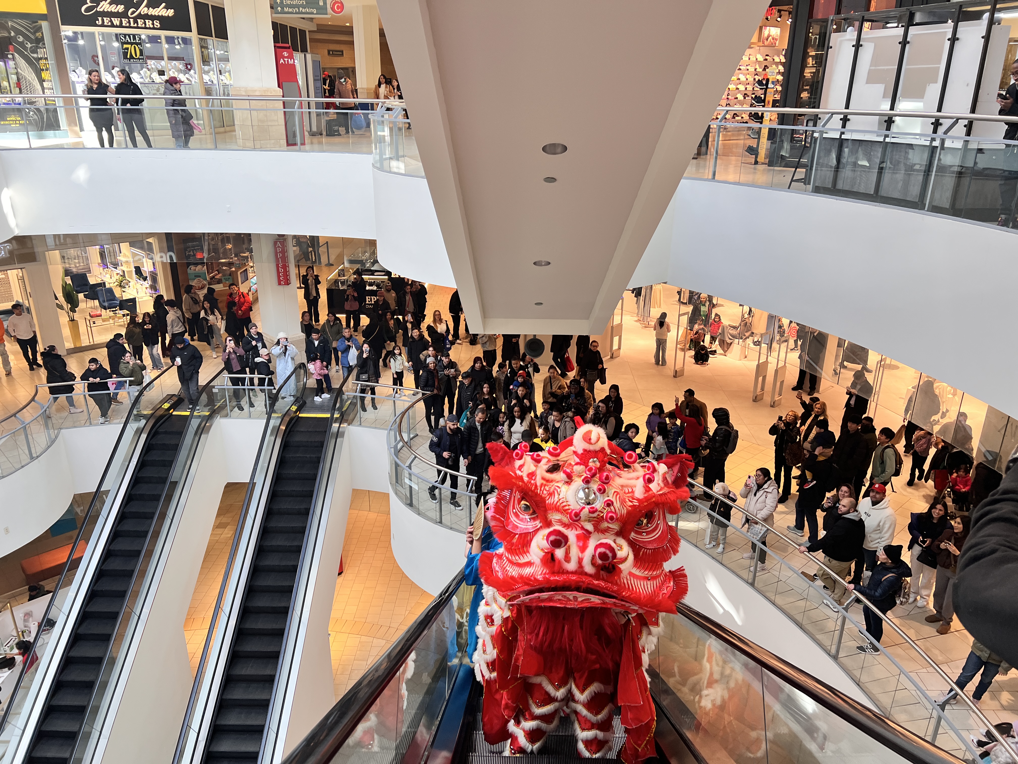 Lion dancer going up escalator to celebrate Lunar New Year with crowd behind them