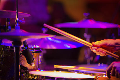 Close-up of a drummer performing on a drum set under colorful stage lighting representing a live music concert.
