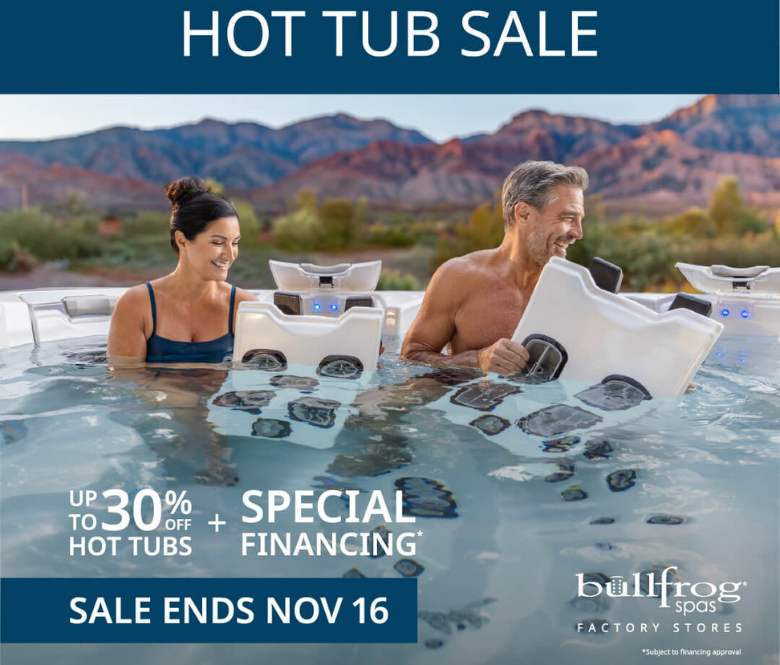 Man and woman sitting in a hot tub smiling with mountains in the background.