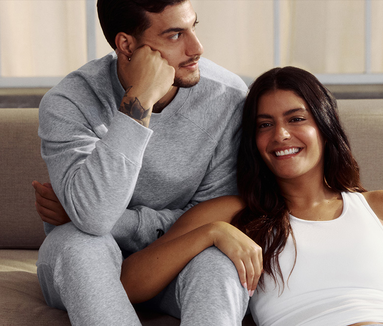 A man and woman pose while seated in gray and white athletic apparel, with the woman leaning comfortably against the man.