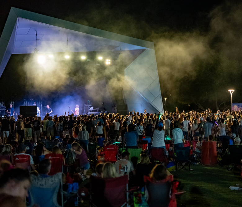 Concert goers in front of a stage watching a band play at night.