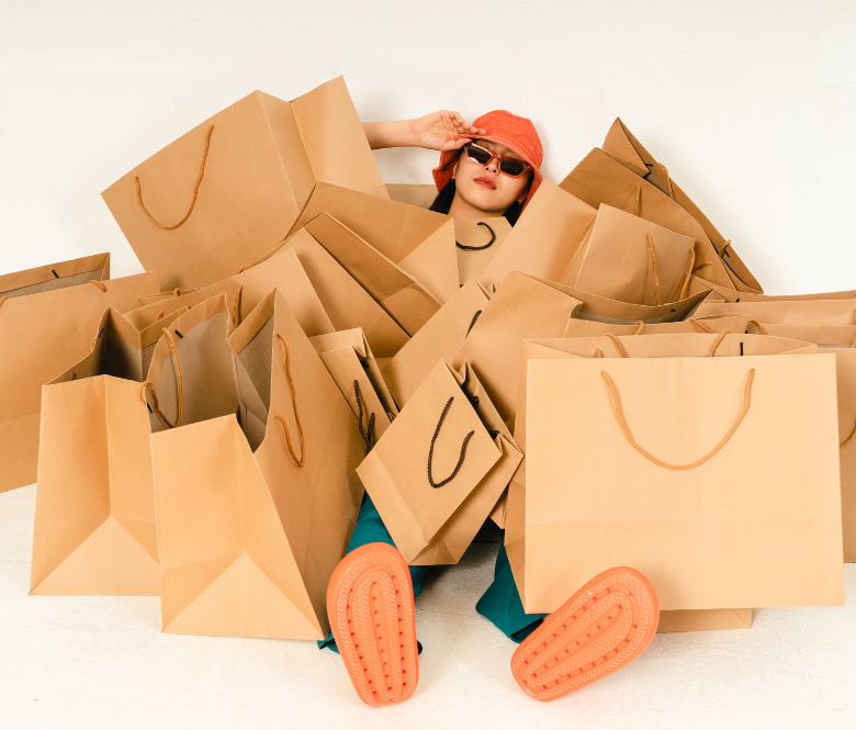 A girl wearing sunglasses underneath a pile of brown shopping bags.
