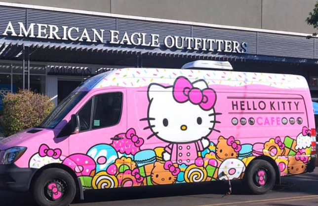 Pink and white van with Hello Kitty and sweet treats painted on the side in front of an American Eagle sign.