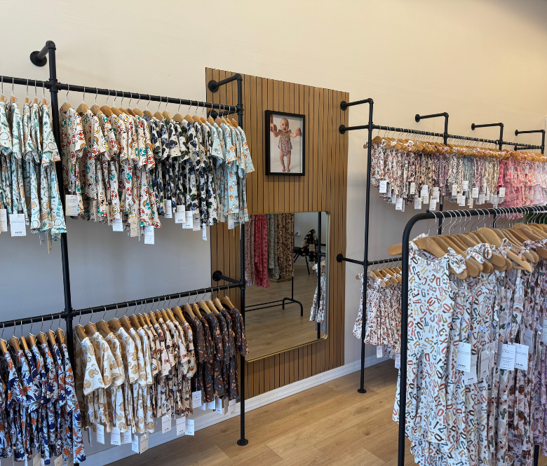 Clothing hanging from racks with a mirror centered on the wall and a picture frame above it.