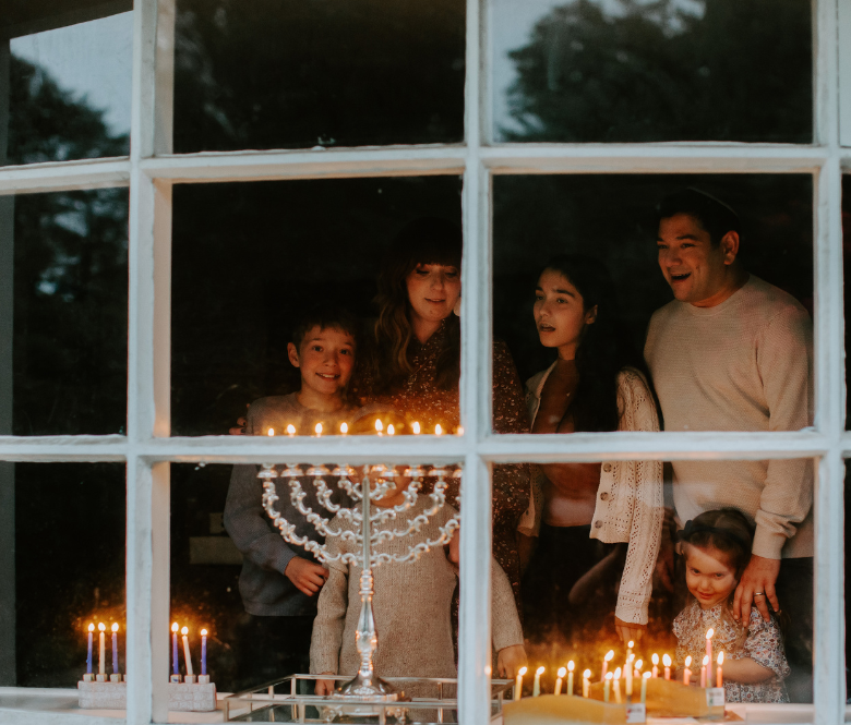 Family gathered around lit Menorahs singing and smiling.