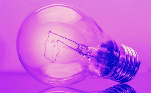 Purple lightbulb on a reflective surface with a purple background.