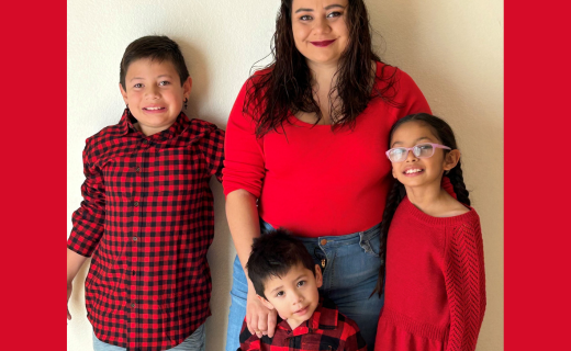 A family of four smiling and dressed in red shirts and sweaters. 