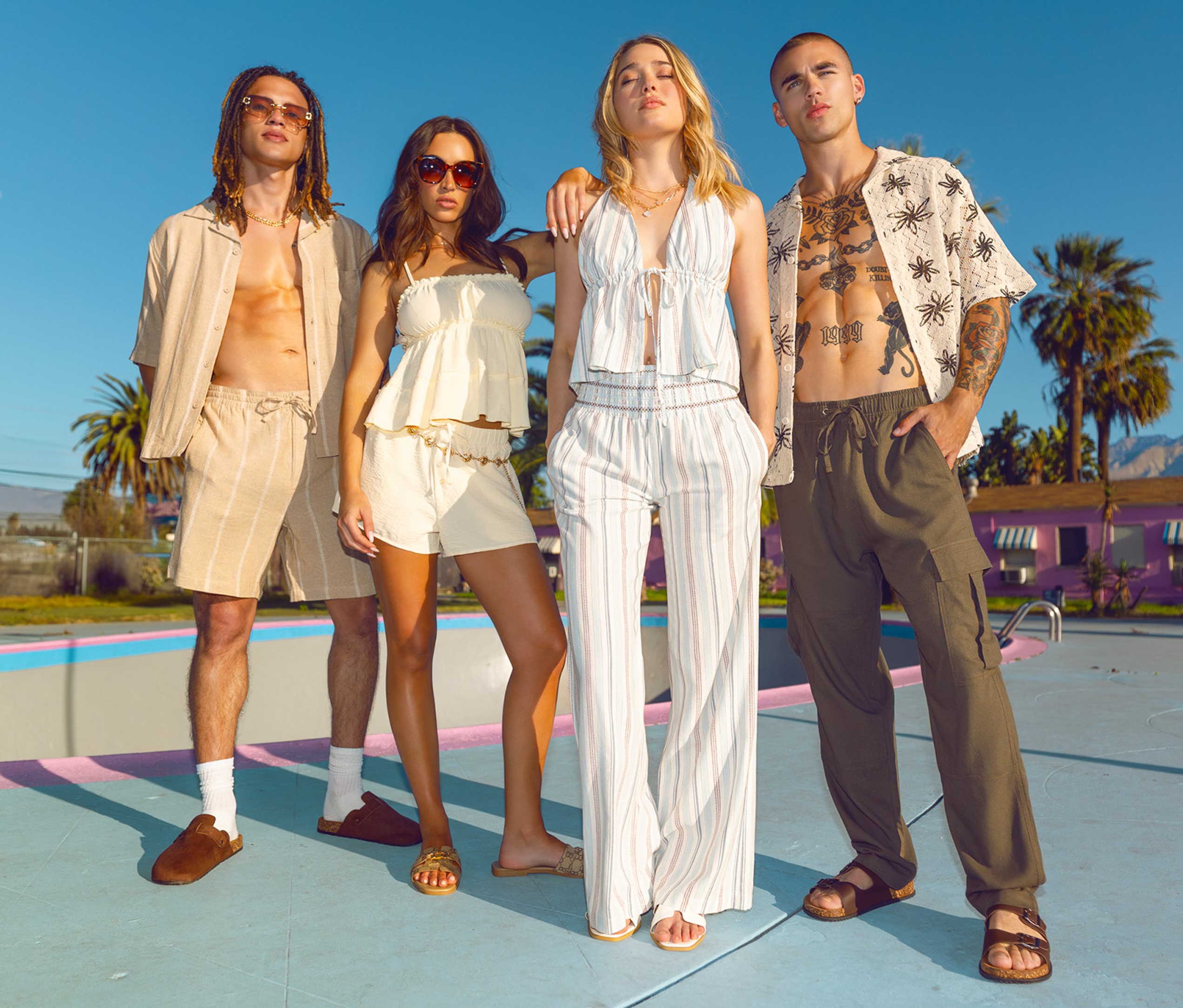 People posing in summer apparel in front of an empty pool.