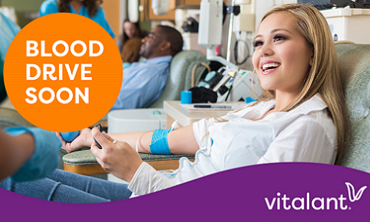 Woman sitting in a chair, giving blood and smiling.