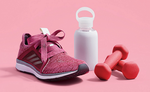 Running shoes, water bottle and weights on a pink background.