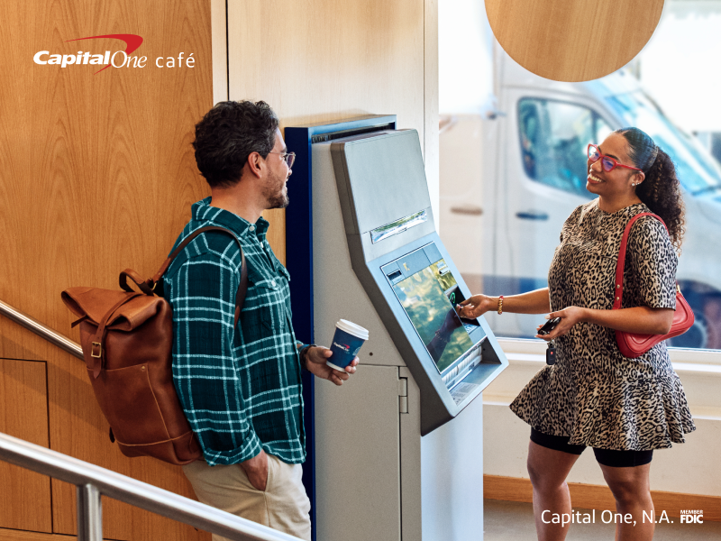 Two people in the lobby of a capital one cafe talking with coffee in hand 