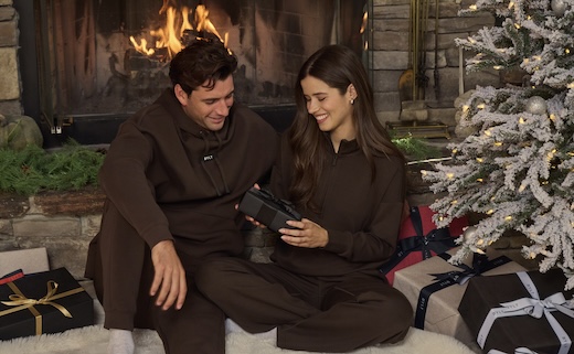 a man and woman smiling while holding a gift in front of a christmas backdrop