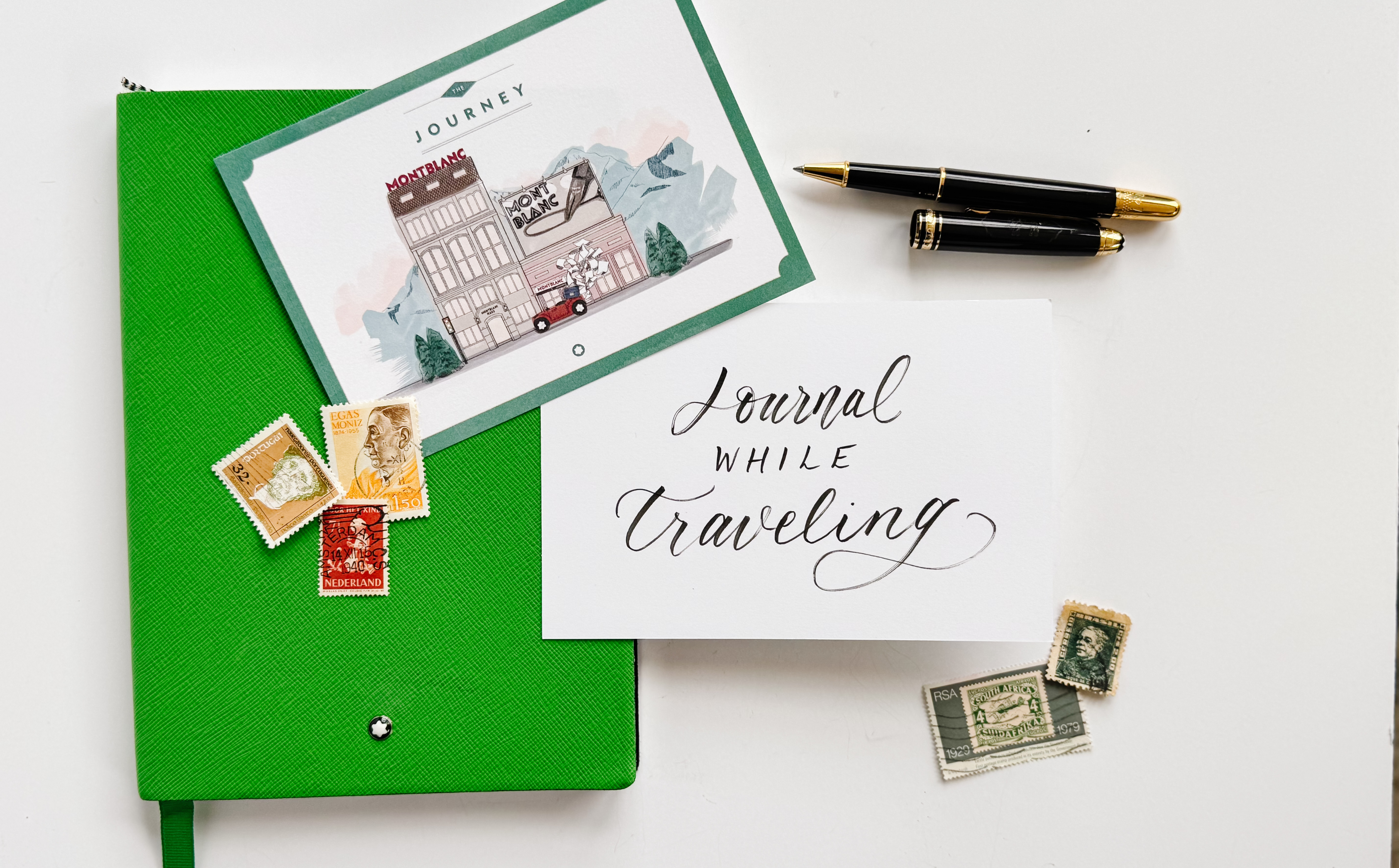 green notebook with stamps, postcards, and pens. note saying "journal while traveling"