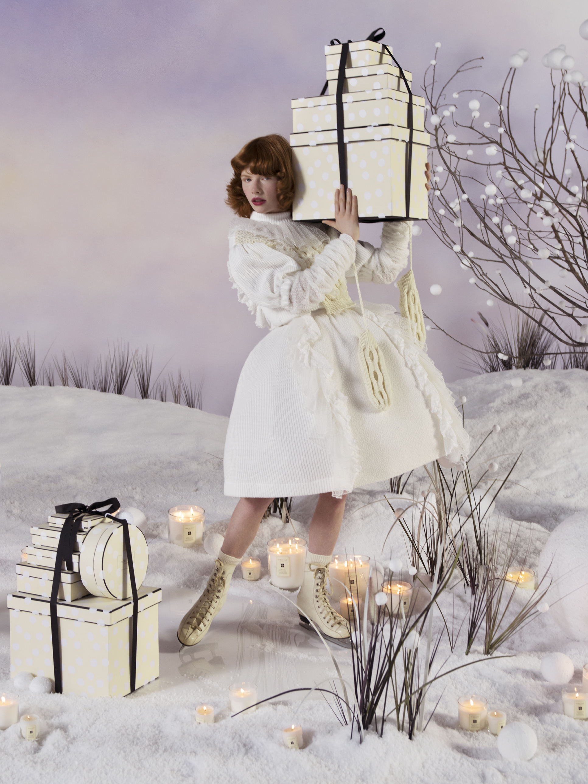 woman in white winter coat with white dress on ice skates holding Jo Malone boxes in a winter wonderland