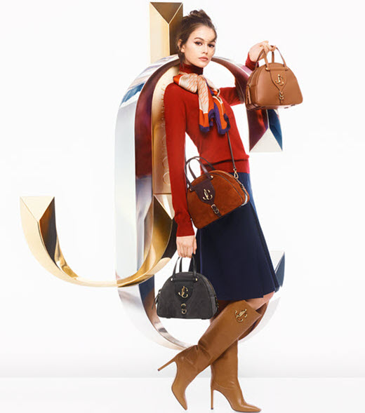 Model carrying three Jimmy Choo bags wearing Jimmy Choo shoes leaning on Jimmy Choo logo