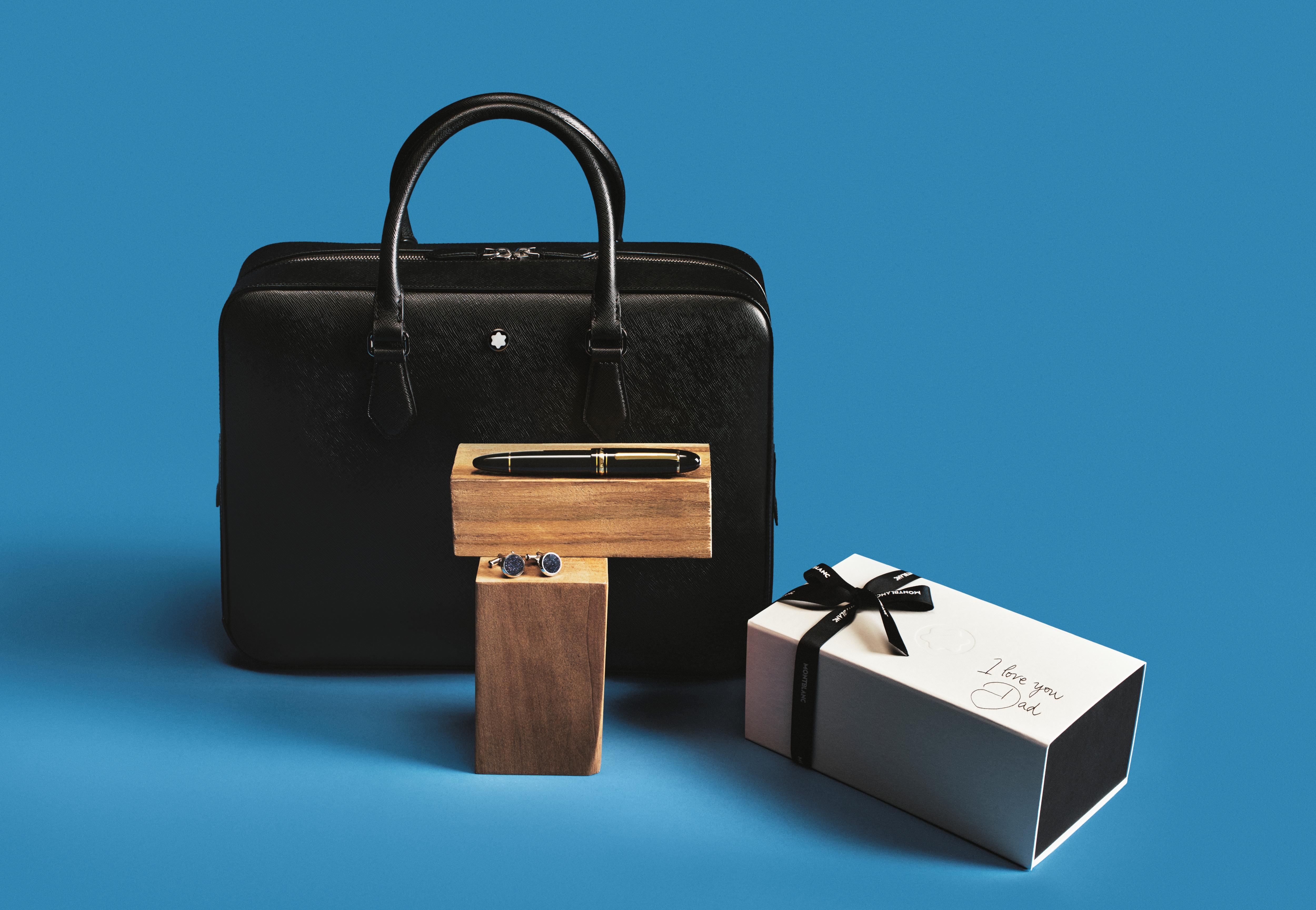 montblanc bag, pen, and cuff links against a blue background with a wrapped present saying "i love you dad"