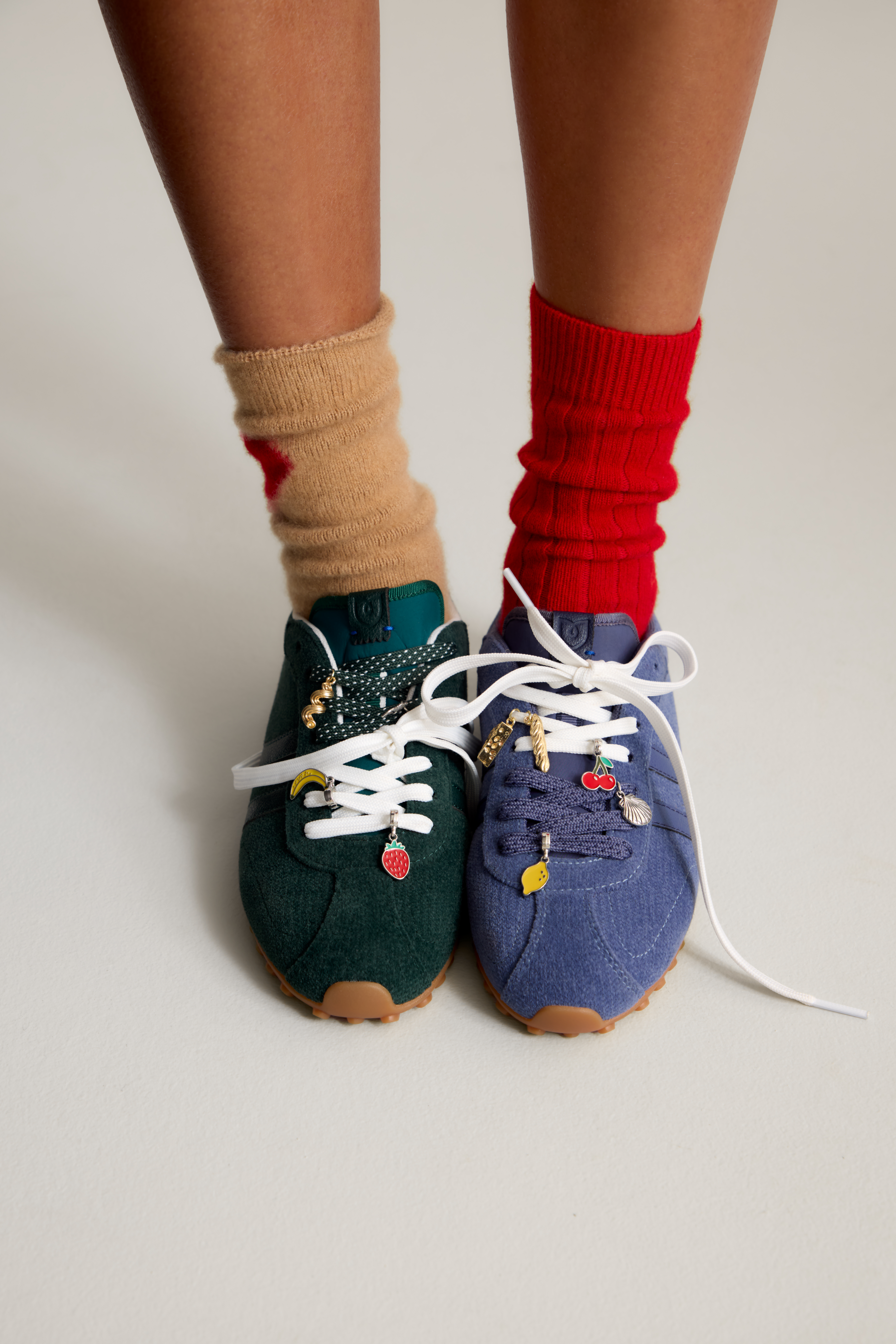 Image of two sneakers - one in a dark green color and one in a ivy blue. there's are little jeweled charms on the shoes laces.
