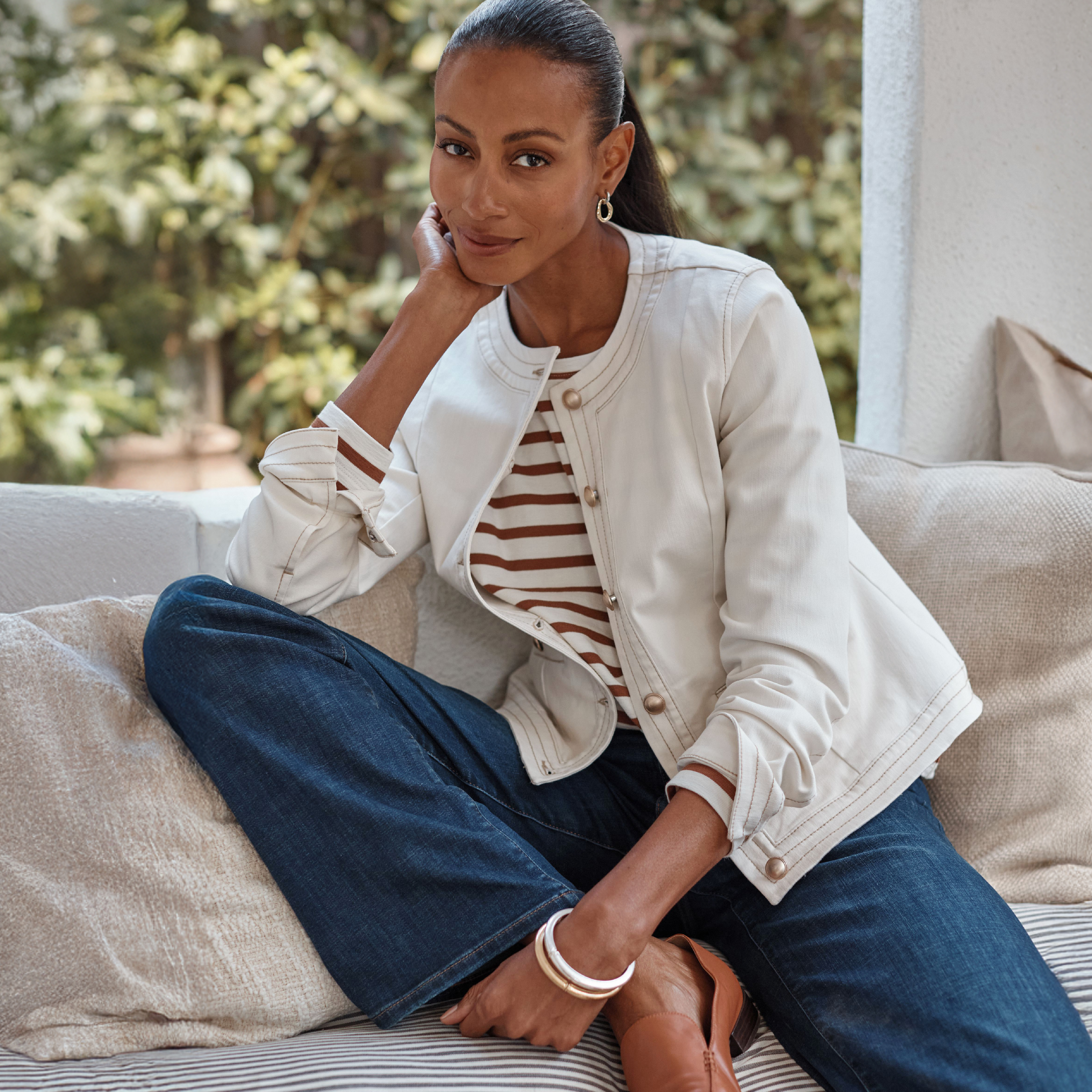 model sitting on a couch in a striped shirt, jeans, and a jacket