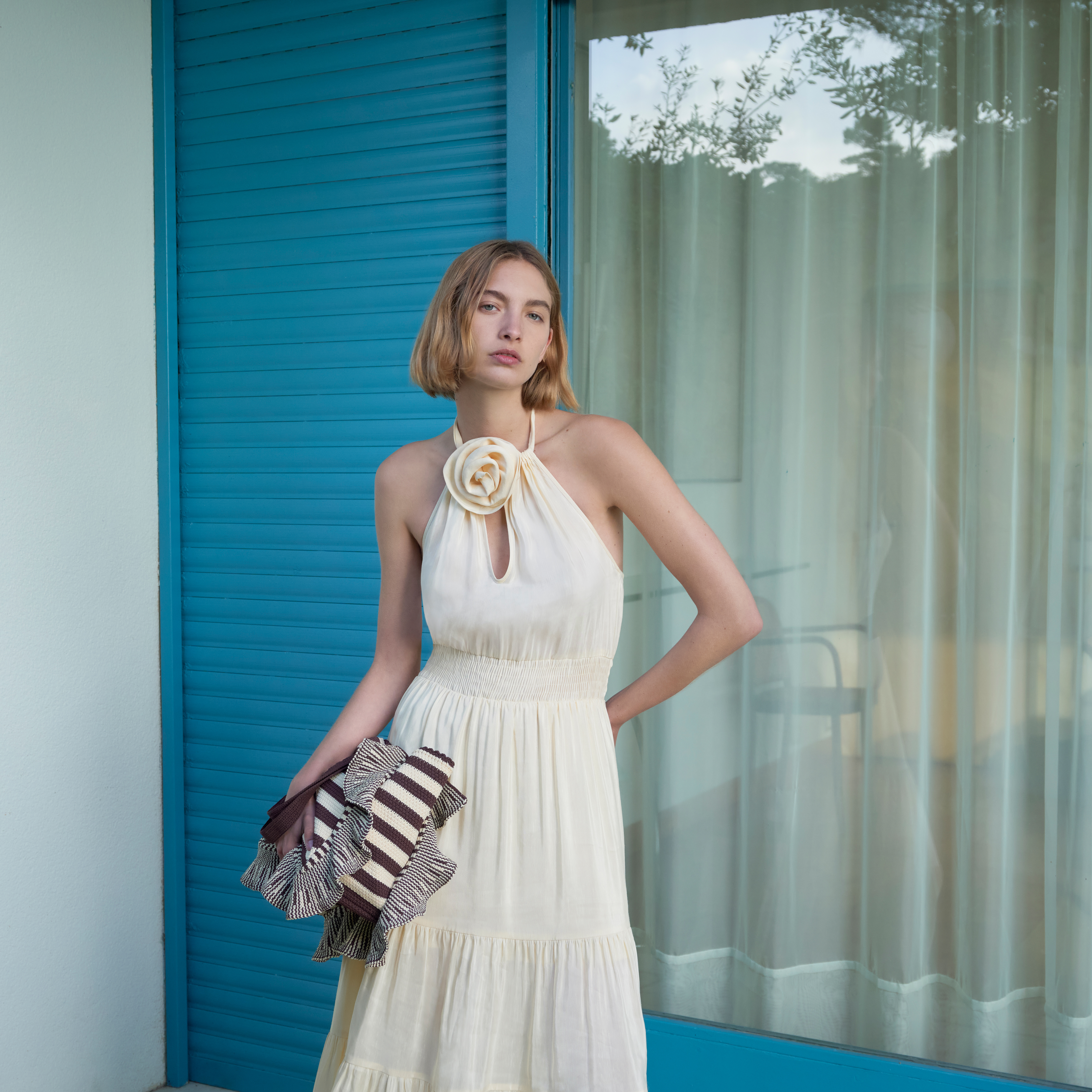Tall blonde lady with short bob hair wearing a light butter cream halter dress and holding a purse