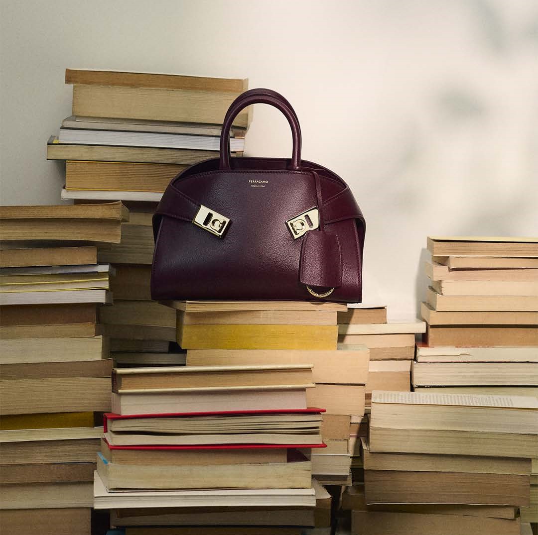 ferragamo bag on top a pile and backdrop of stacked books 