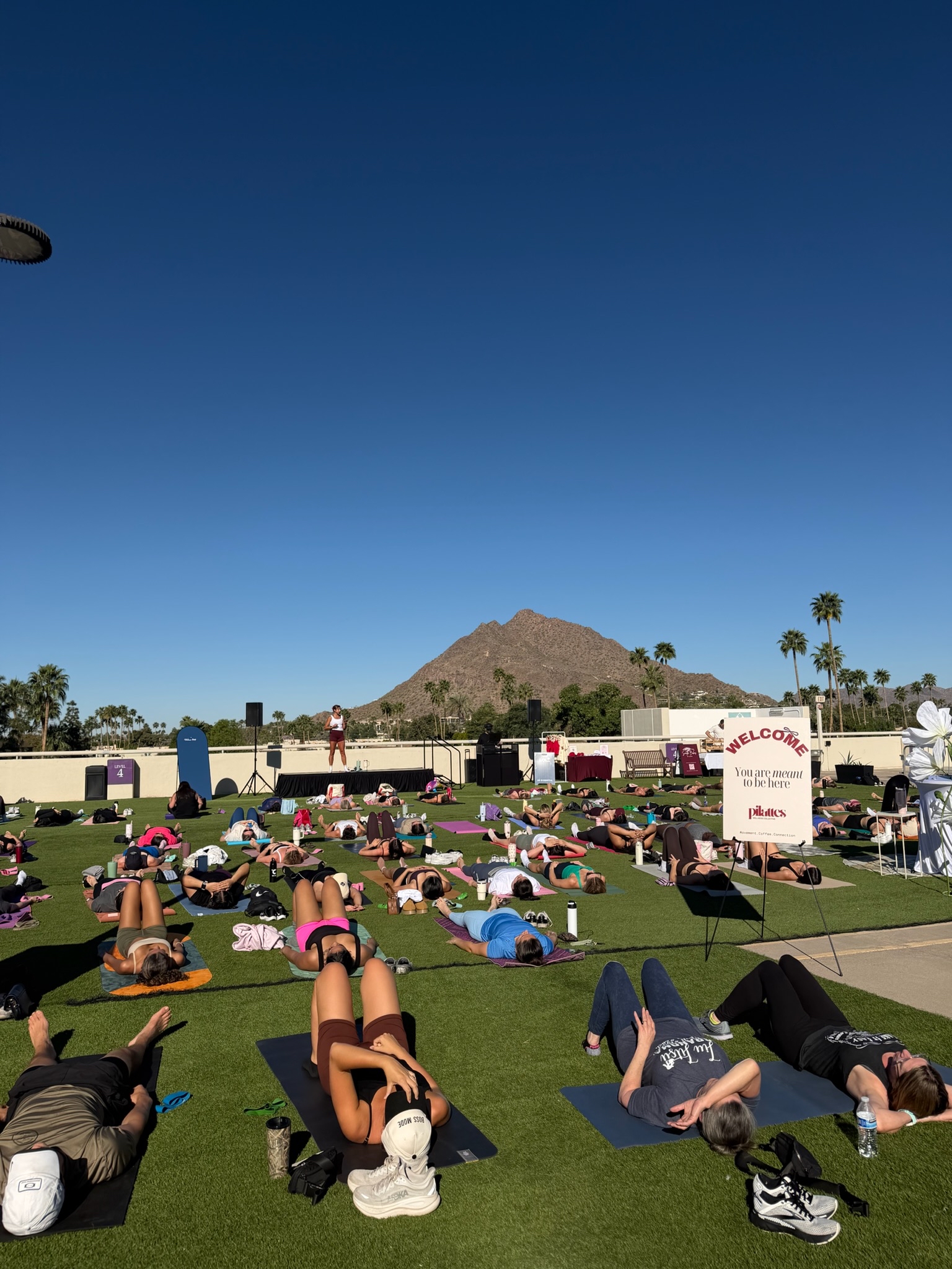 rooftop class with people on mats with the instructor talking against the blue sky and mountain backdrop