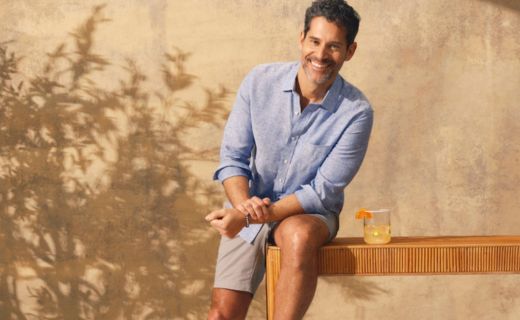 male model leaning on table smiling with a fruity drink next to him 