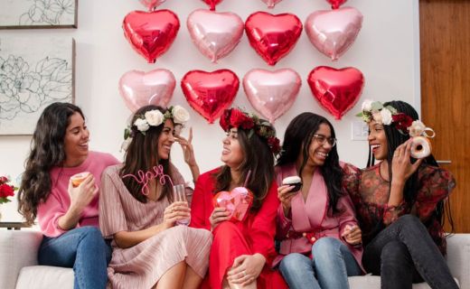 group of girls laughing on a couch with heart balloons in the background 