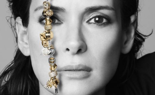 close up view of a woman's face holding a gold and silver bracelet in front of it