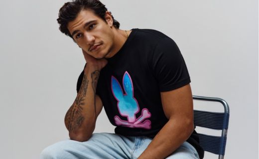 male model sitting in chair wearing a black shirt with psycho bunny logo on it