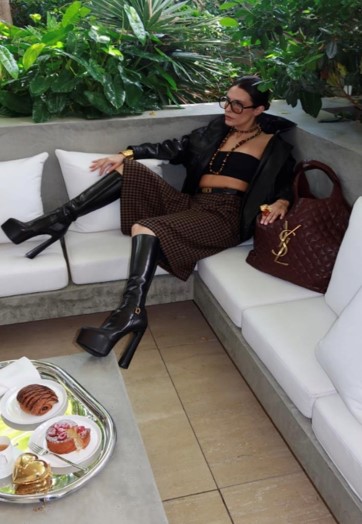 model posing on couch with ysl bag and breakfast spread on table in front of her
