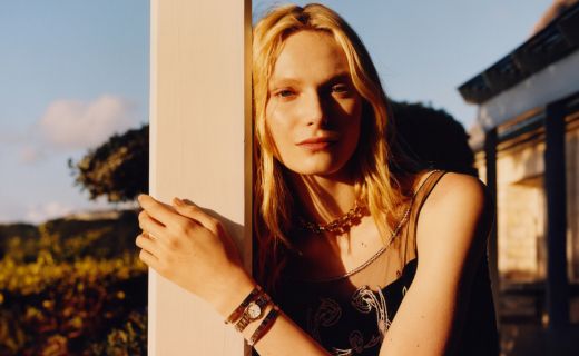 model leaning against a post showing off a watch and bracelets on her wrist 