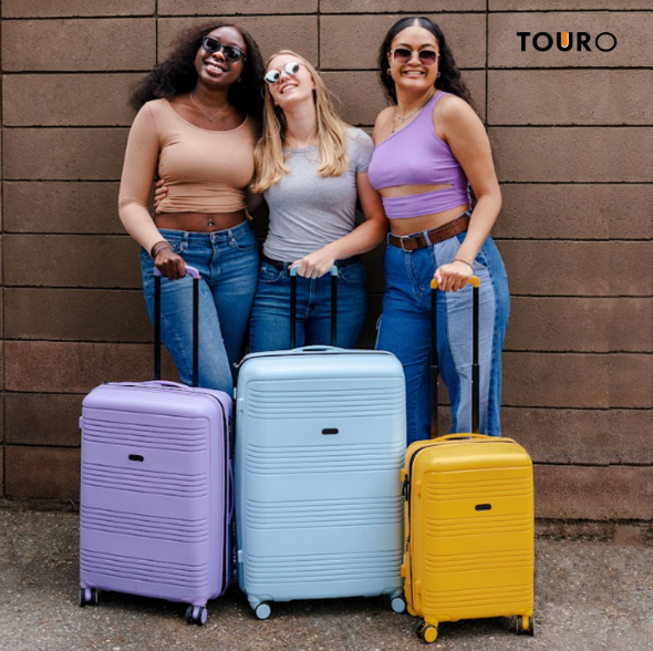 three girls smiling and posing with pastel colored luggage. touro logo
