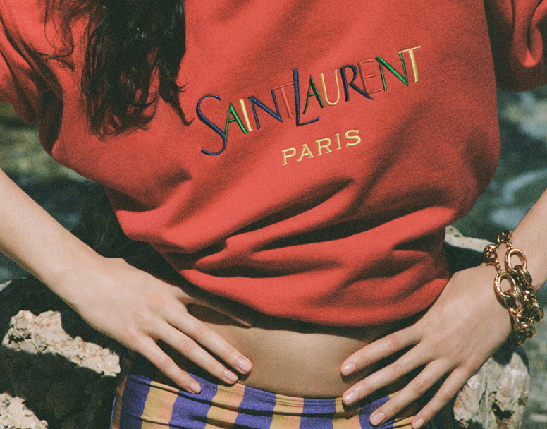 female model wearing a red sweatshirt with the words Saint laurent Paris - accessorized with two gold chain bracelets 