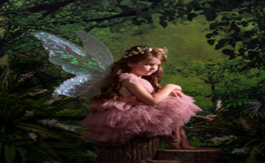 Girl dressed in a fairy costume with wings surrounded by lush greenery and trees.
