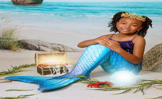 Girl dressed as a mermaid sitting by the ocean with a jewelry chest.