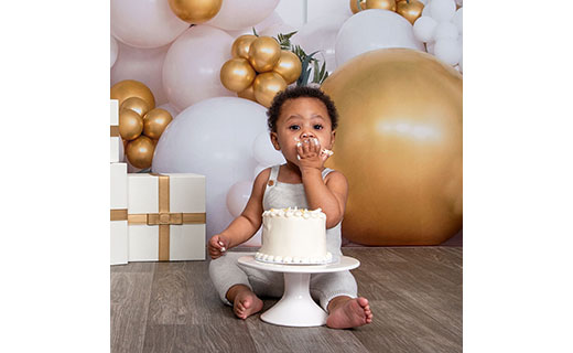 Little girl celebrating with birthday cake and balloons and presents in the background.