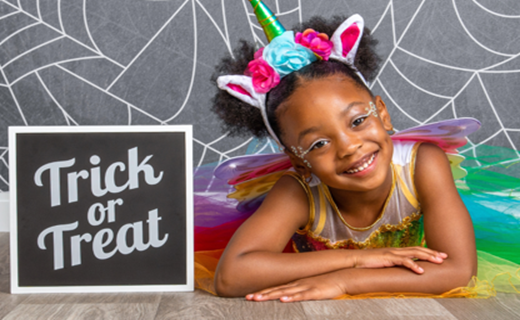 Girl with wearing fairy costume with floral bunny ear headband in front of a spider web backdrop with a sign that says Trick or Treat