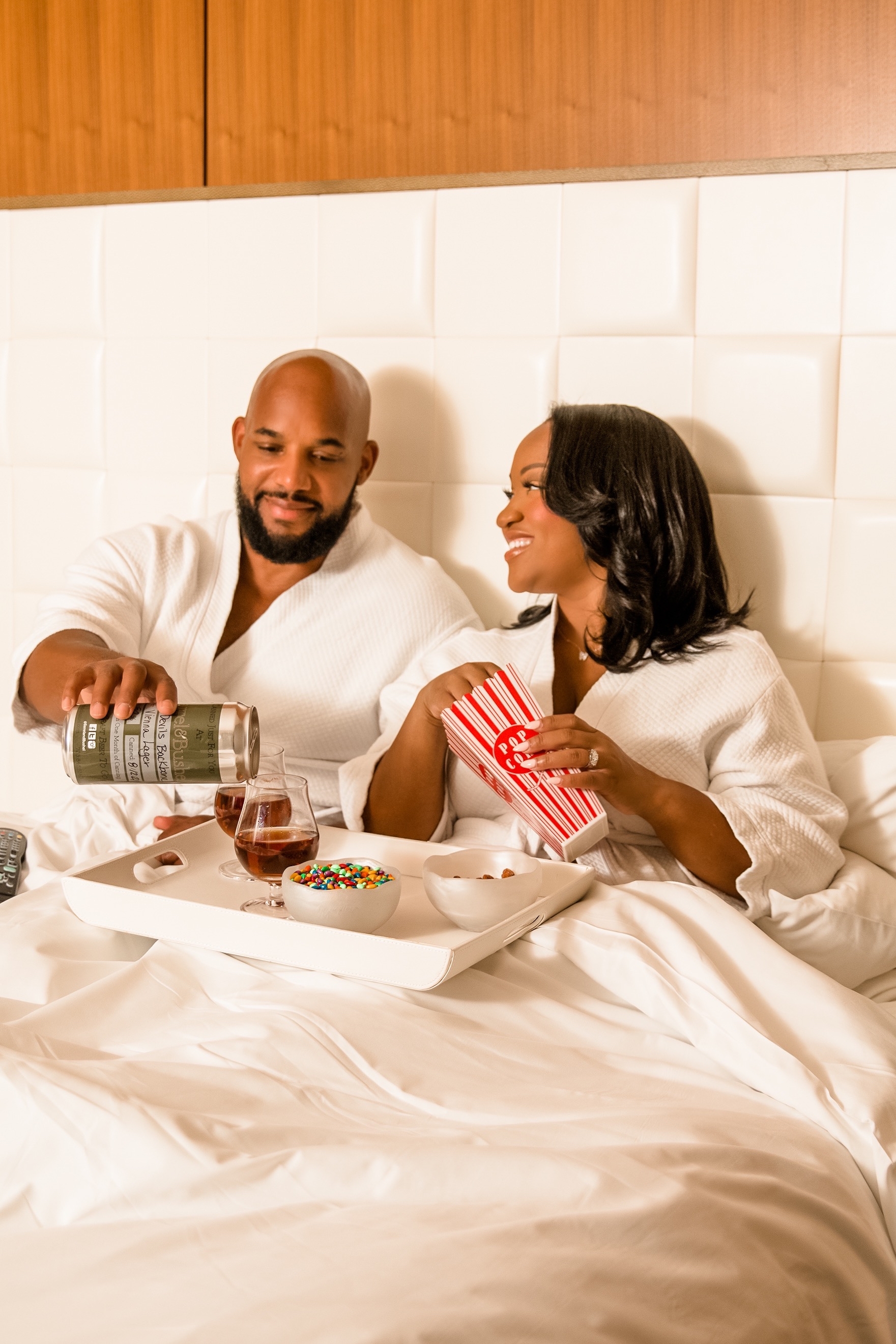 couple wearing hotel robes eating movie snacks in bed 