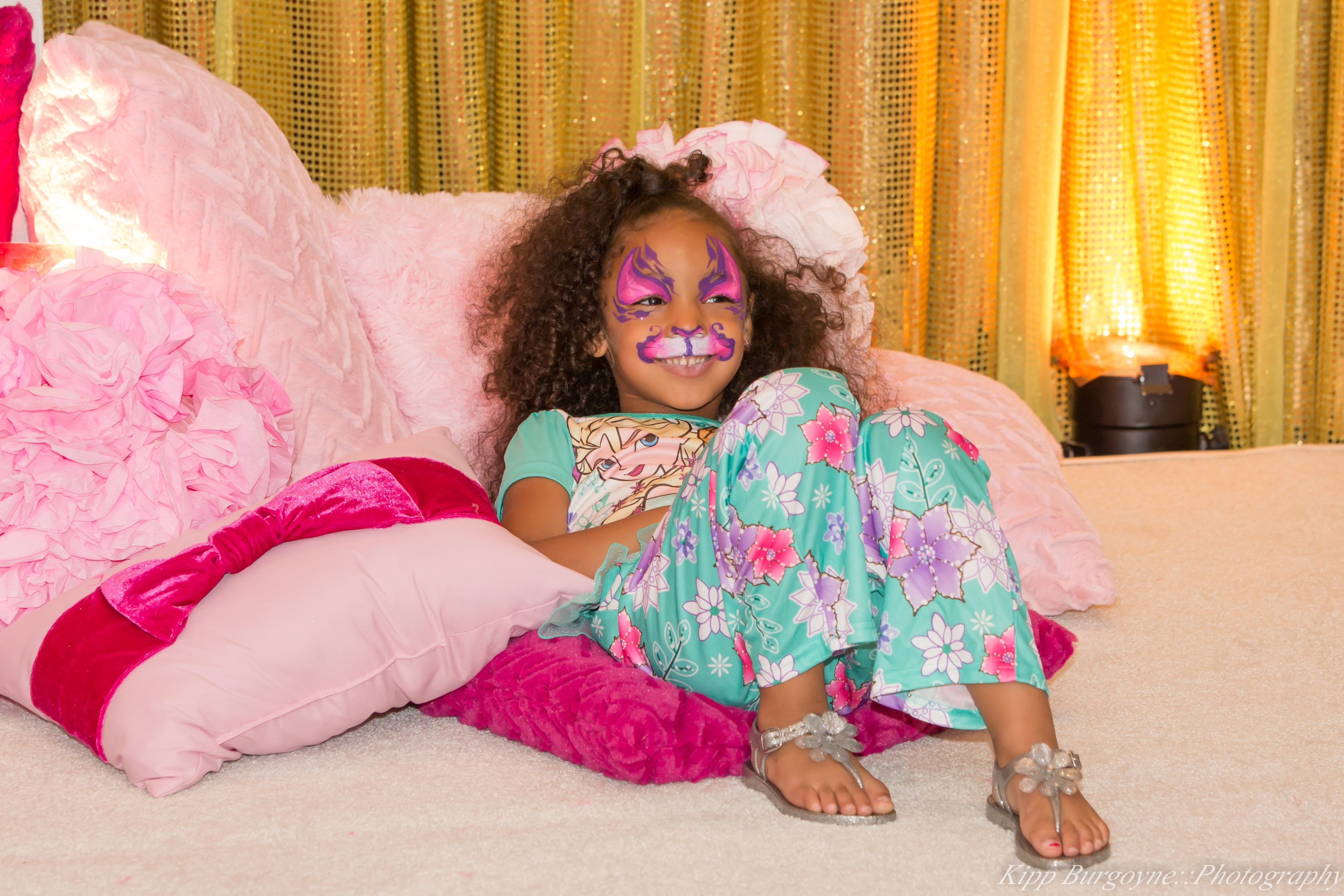 young girl with glam face paint surrounded by plush pillows wearing pajamas 